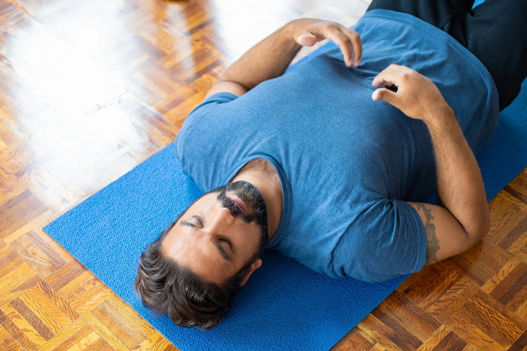 An adult lying on a blue mat with the knees bent