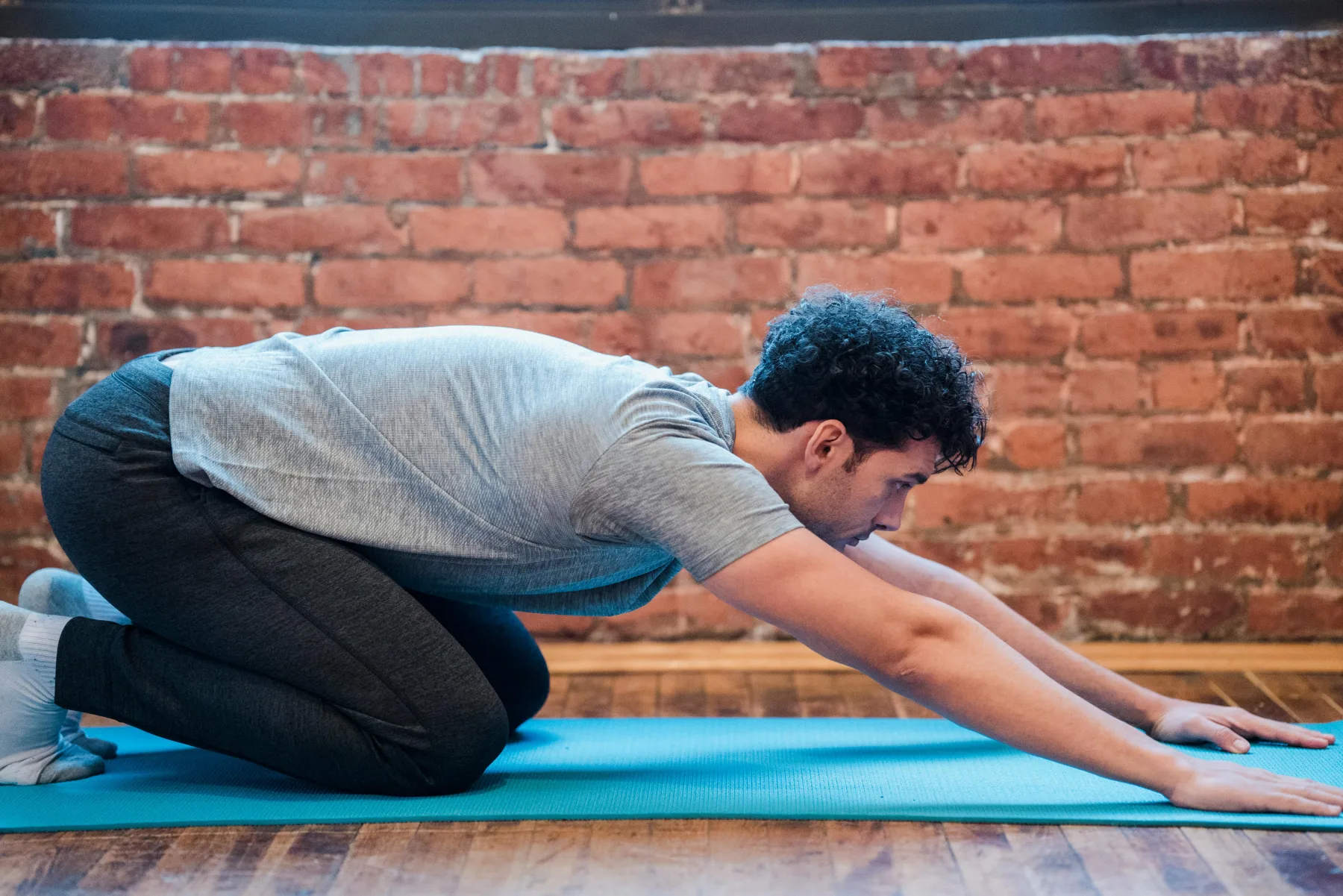 An adult kneeling on a mat with the arms reaching forward